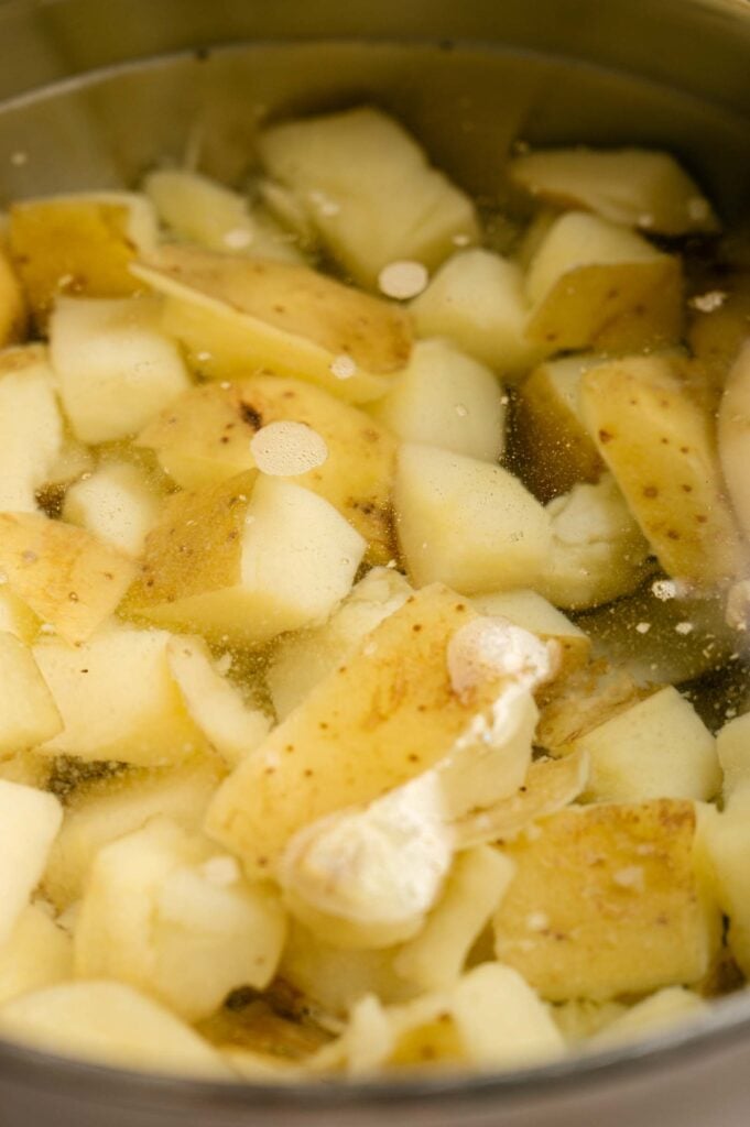 Cubed potatoes with skins on are submerged in water inside a metal pot, small bubbles forming on the surface—the first step in preparing classic Southern Potato Salad.