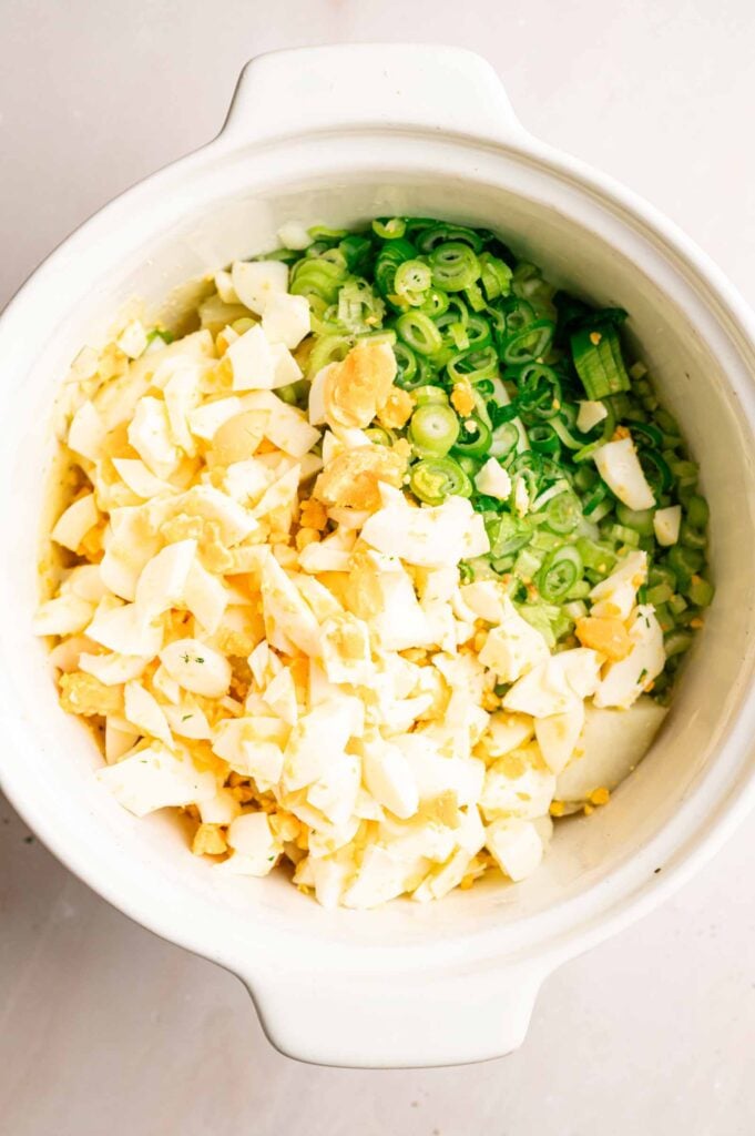 Chopped hard-boiled eggs and sliced green onions in a white bowl on a light surface, perfect for adding to Southern Potato Salad.