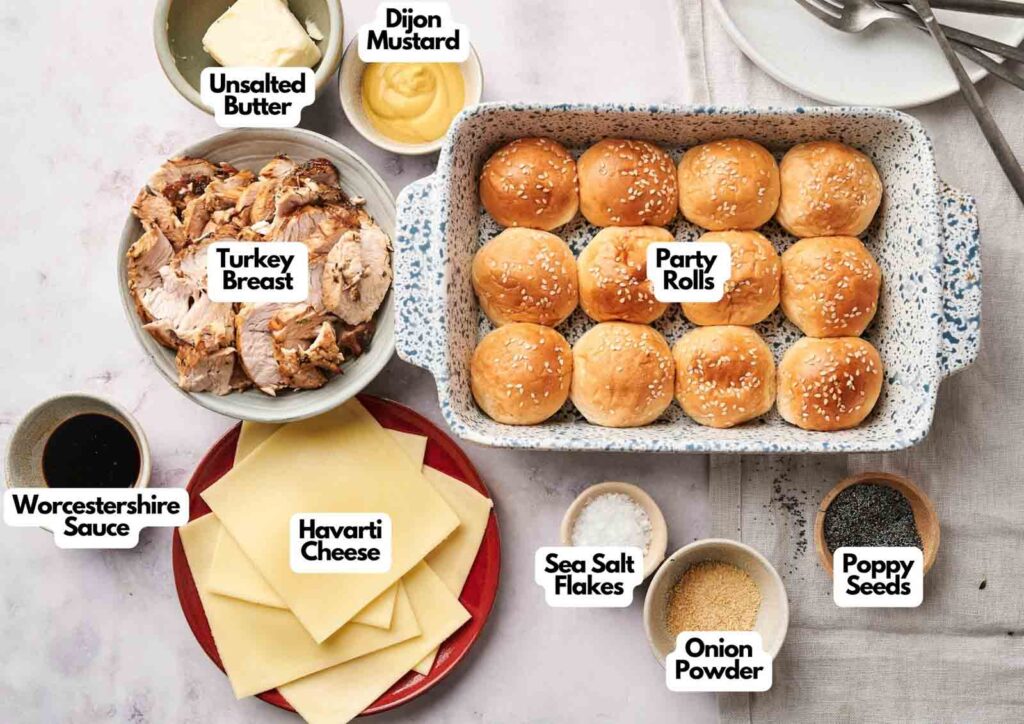 A top-down view of Air Fryer Turkey Sliders ingredients, including turkey breast, party rolls, havarti cheese, butter, dijon mustard, Worcestershire sauce, sea salt flakes, onion powder, and poppy seeds.