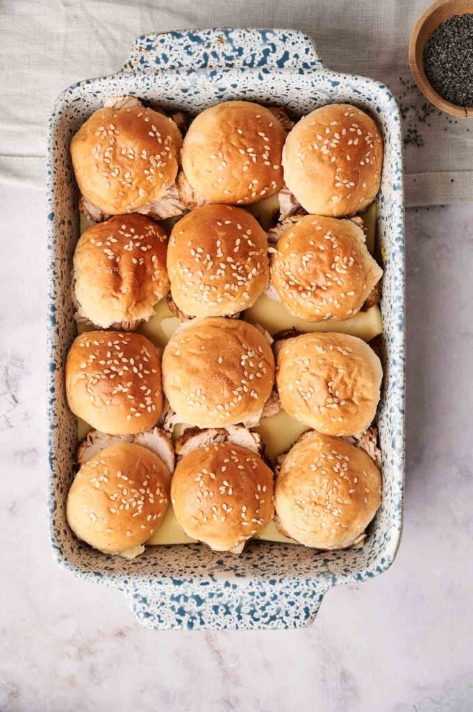 A rectangular baking dish filled with twelve sesame-topped Air Fryer Turkey Sliders arranged in neat rows.